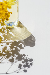 Transparent glass bottle of oil or cosmetic serum. Focus on shadow. White background with daylight and beautiful shadows with yellow flower.