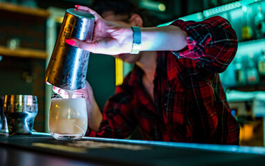 bartender hand pouring a cocktail into a glass in bar