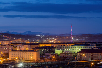 Evening city landscape. Buildings and TV tower view. Mountains in the distance. Evening twilight. Magadan, Magadan Region, Siberia, Russia.
