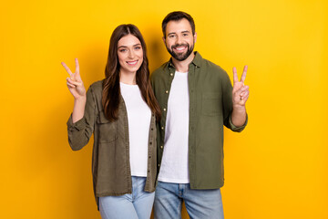 Portrait of two positive cheerful people hand fingers demonstrate v-sign isolated on yellow color background