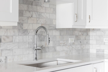 A kitchen sink detail shot with white cabinets and a marble subway tile backsplash.