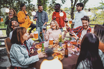 Fototapeta na wymiar Young friends having fun drinking beer and wine on balcony at farmhouse dinner pic nic party - Hipster millennial people eating bbq food at fancy restaurant together - Dinning life style concept