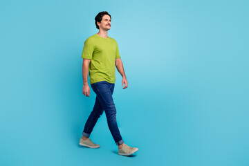 Fototapeta na wymiar Full length photo of pretty attractive guy dressed green t-shirt walking looking empty space isolated blue color background