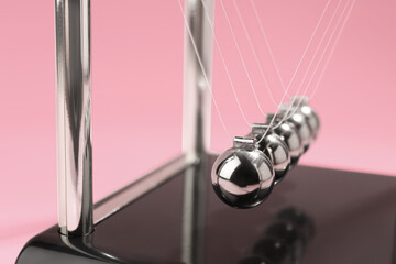 Newton's cradle on pink background, closeup. Physics law of energy conservation