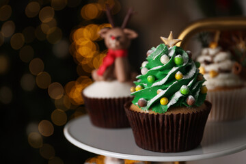 Christmas tree shaped cupcake on white stand against blurred festive lights, space for text