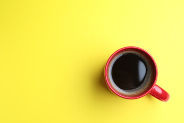 Fresh aromatic coffee in red mug on yellow background, top view. Space for text