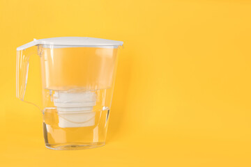Filter jug with purified water on yellow background. Space for text