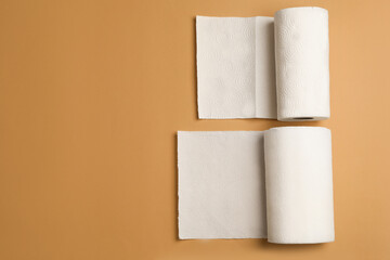 Rolls of white paper towels on brown background, flat lay. Space for text