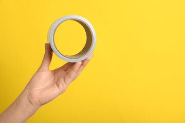 Woman holding adhesive tape on yellow background, closeup. Space for text