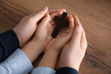 Boy and his godparent holding cross at wooden table, closeup