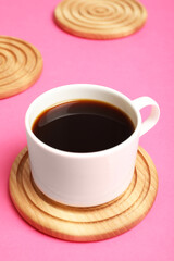 Cup of coffee and stylish wooden coaster on pink background, closeup