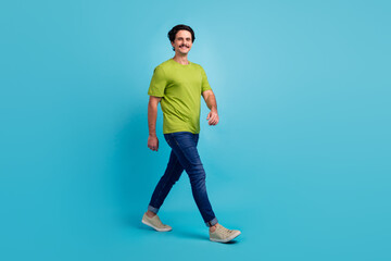 Fototapeta na wymiar Full length photo of sweet positive man wear green t-shirt walking empty space smiling isolated blue color background