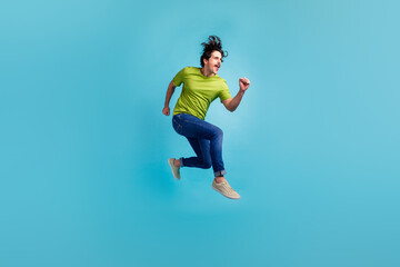 Fototapeta na wymiar Full length photo of attractive purposeful guy dressed green t-shirt jumping high running fast isolated blue color background