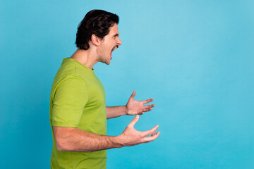 Photo of shocked angry man wear green t-shirt looking empty space screaming isolated blue color...