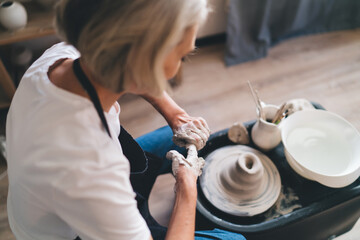 Female sculptor making clay pot on pottery wheel