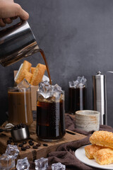 Pour milk make latte coffee, Asian iced coffee in transparent glass and roasted coffee beans and Crispy Pie on wood. black background studio photo, Copy space for your text