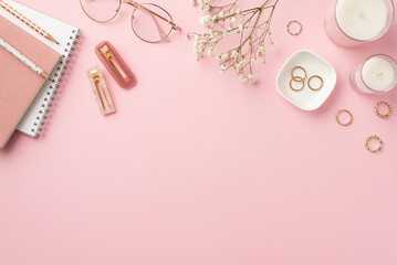 Business concept. Top view photo of workspace candles notebooks pencils stylish glasses gold rings trendy barrettes and white gypsophila flowers on isolated pastel pink background with copyspace