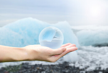 Crystal sphere in hand with iceberg background. World environment day, global warming and climate...