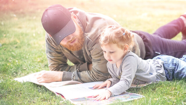 View of bearded man and a blond-haired girl on sunny day and read a book.