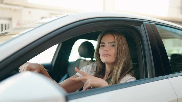 Young woman doing victory gesture with fingers sitting on car at street