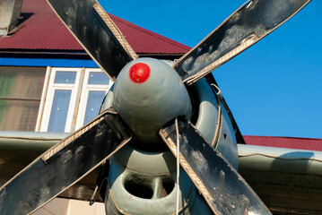 a large old stripped propeller of an airplane against the background of a house and a blue sky