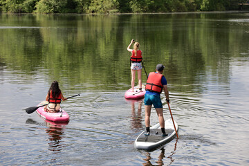 Sup surfing, man and two girls with paddles sailing on a boards in river. Stand up paddle boarding in summer - obrazy, fototapety, plakaty