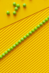 top view of line and scattering of green balls on textured yellow background.