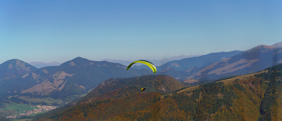 Paraglider flying in the blue sky with mountain in background.