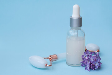 Serum with flower extracts for skin care and lilac flowers, face massage roller on a blue background. copy space