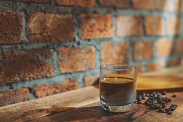 A Glass of Dirty coffee by espresso shot topped over cold fresh milk create a gradient layer in the morning over a red bricks wall background and coffee beans on a wooden Cafe table. For Copy Space