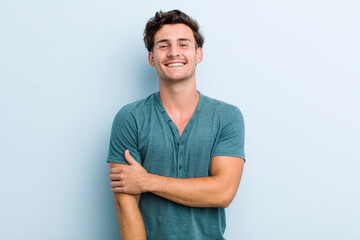 young handsome man laughing shyly and cheerfully, with a friendly and positive but insecure attitude