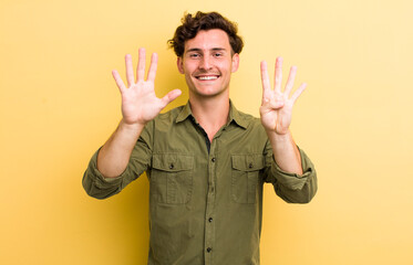 young handsome man smiling and looking friendly, showing number nine or ninth with hand forward,...