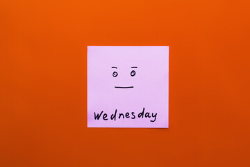 top view of paper note with wednesday lettering and calm smiley on orange background.