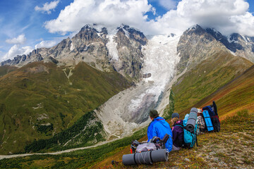 Three tourists with big backpacks looks at the Adishi Lardaad glacier in Georgia. Svaneti.