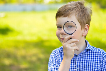 A schoolboy boy explores nature with a magnifying glass. Summer holidays for curious children in the forest. Hiking. Future scientist botanist