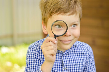 A schoolboy boy explores nature with a magnifying glass. Summer holidays for curious children in...