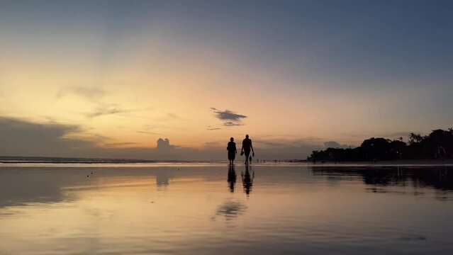 Live camera view of silhouettes of a loving couple on wet beach sand reflecting tropical sunset above the ocean. Anonymous people enjoying peaceful seaside.