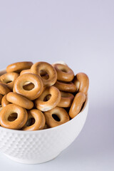 Small Crispy Bagels in a White Ceramic Bowl on a Blue Background Vertical Tasty Snack