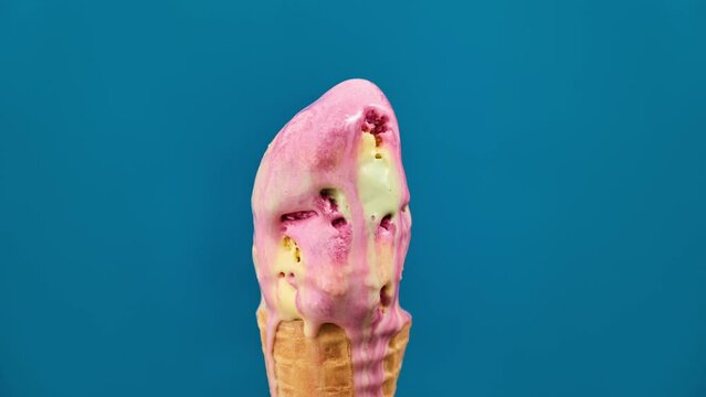 Delicious ice cream with different colors in waffle cone melting. Timelapse of red, yellow, green ice cream melting on blue background. Close-up of sweet dessert. Yummy food. 4K, UHD