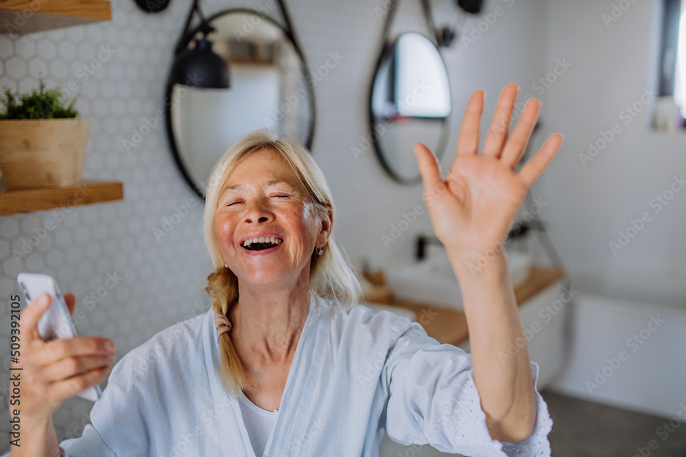 Poster Cheerful senior woman in bathrobe listening to music in bathroom, relax and wellness concept.