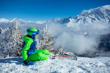 Ski boy sit looking on top of the mountain covered by clouds