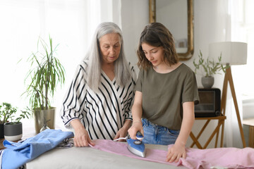Teenage girl ironing and helping with household chores her senior grandmother at home