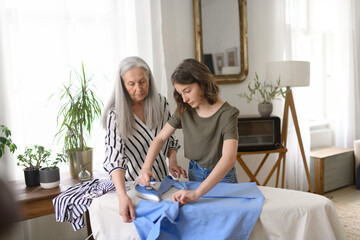 Teenage girl ironing and helping with household chores her senior grandmother at home