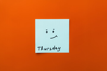 top view of sticky note with thursday inscription and positive smiley on orange background.