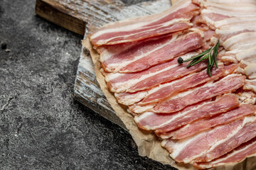Bacon slices and rosemary on a wooden board, Keto diet food ingredients. Food recipe background. Close up
