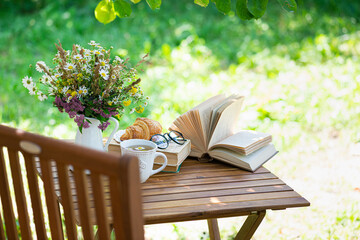 Bouquet of meadow flowers, croissant, cup of tea or coffee, books on table in summer garden. Rest in garden, reading books, breakfast, vacations in nature concept. Summertime in garden on backyard