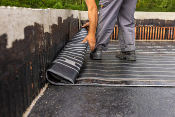 Worker laying the vapor barrier for the roof, bituminous membrane to be welded with flame