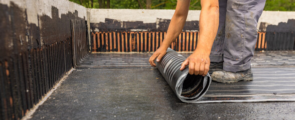 Worker laying the vapor barrier for the roof, bituminous membrane to be welded with flame