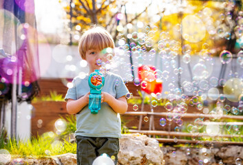 Blond handsome boy play with soap bubbles holding bubble gun