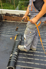 Workers placing a vapor barrier on the roof using a propane gas torch for welding bitumen sheets